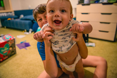 Laughing older brother holding smiling younger brother in his arms in their house