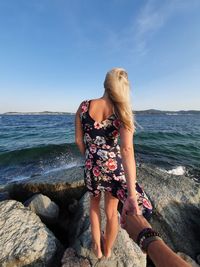 Young woman on rock at beach against sky