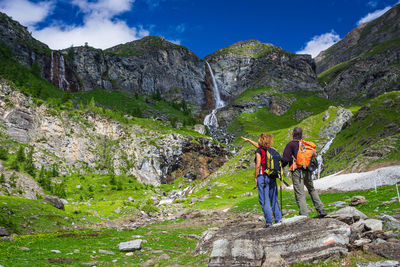 Rear view of men standing on rock against mountains