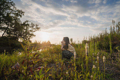 Woman sitting on grass in field against sky