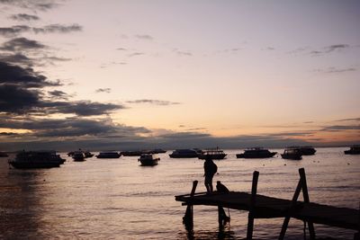 Silhouette people on sea against sky during sunset