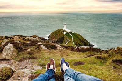 Low section of men standing on cliff by sea against sky