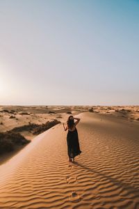 Full length of woman standing on sand dune in desert against sky