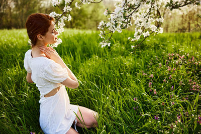Side view of young woman sitting on grassy field