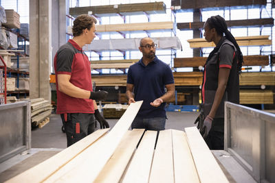 Mature male customer holding plank while discussing with sales staff at hardware store