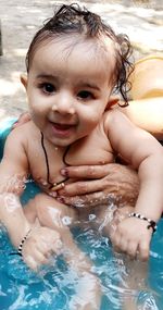 Cropped hands of woman holding naked baby in bathtub