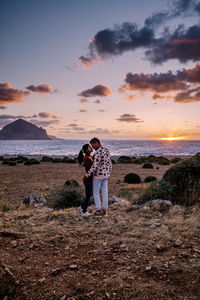 Friends standing on shore against sky during sunset