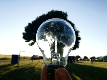 Close-up of hand holding glass on field against sky