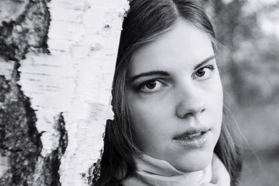 Close-up portrait of smiling young woman against tree trunk