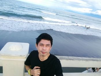 Portrait of smiling man standing at beach against sky