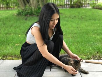 Young woman feeding cat while crouching on footpath in park