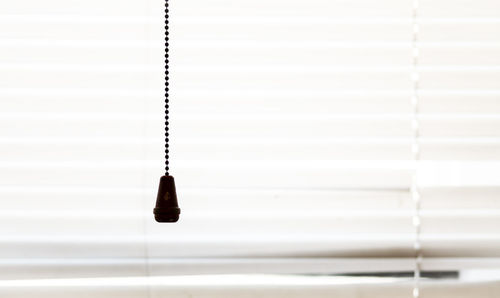 Close-up of string hanging against white blinds