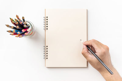 Cropped hand holding pencil on spiral notebook against white background