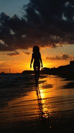 Silhouette woman standing on beach against sky during sunset
