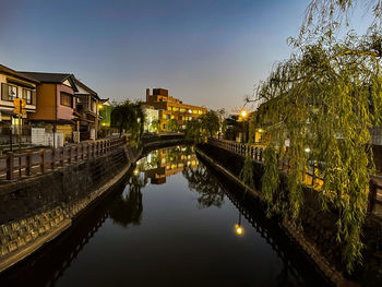 Canal amidst illuminated japanese buildings against sky in city