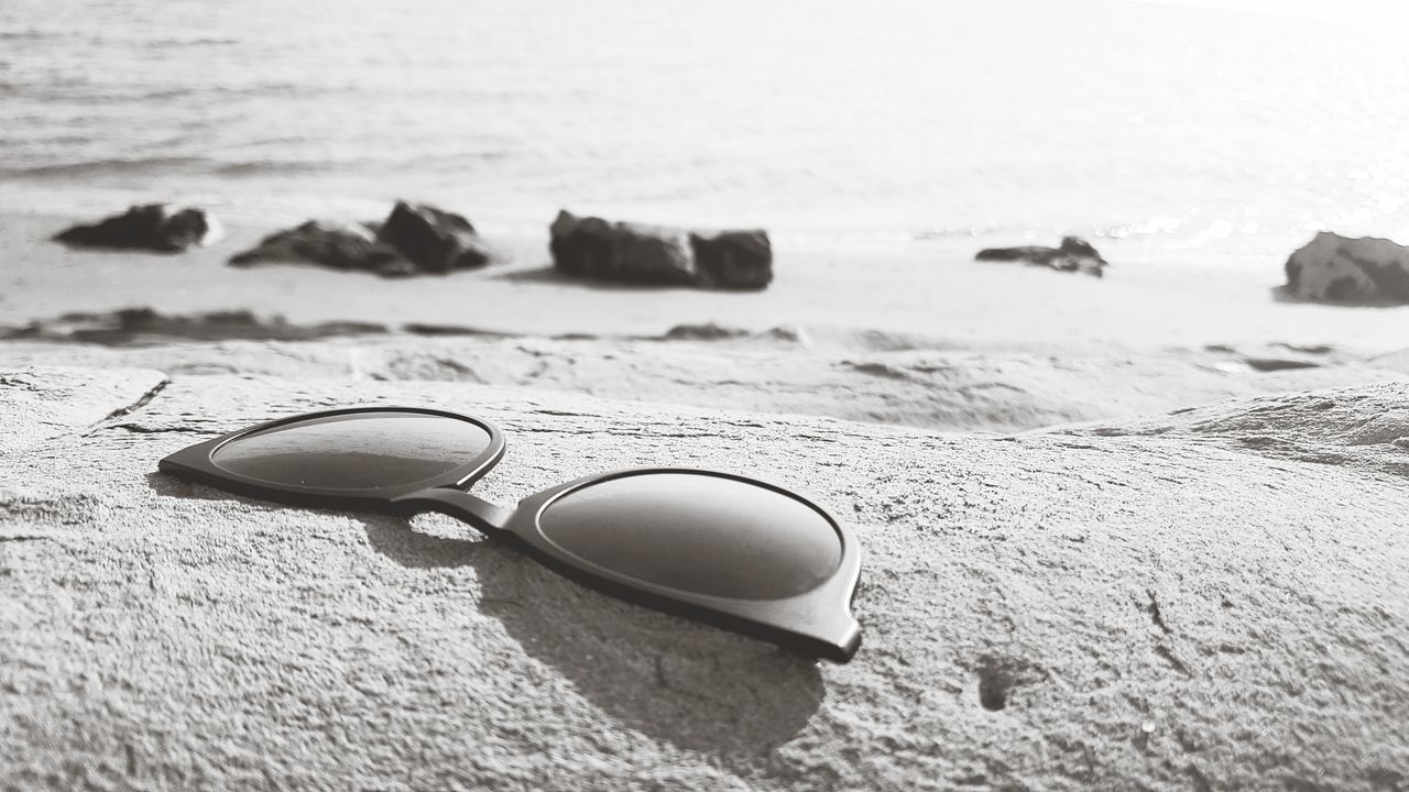 CLOSE-UP OF SUNGLASSES ON SEA SHORE