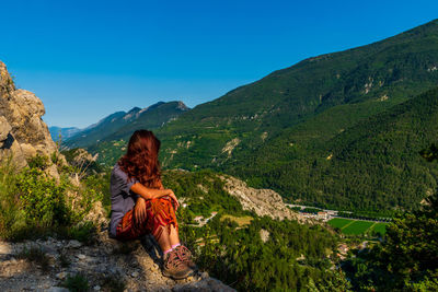 Woman sitting on rock looking at mountains against sky