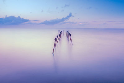 Wooden posts in sea against sky during sunset