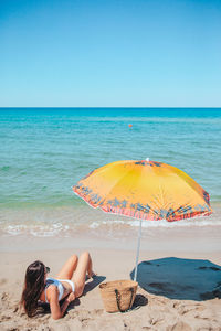 Rear view of woman holding umbrella at beach against clear sky