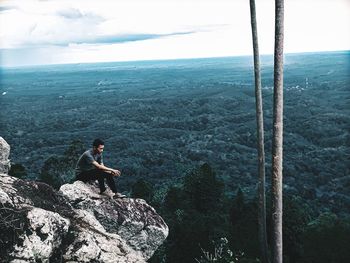 Thoughtful man sitting on rock with landscape in background against sky