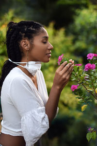 Young woman takes face mask off to smell the flowers