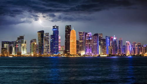 Sea by illuminated buildings against sky at dusk