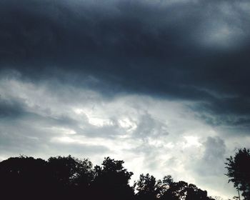 Low angle view of silhouette trees against cloudy sky