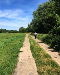 Rear view of people on road amidst field against sky