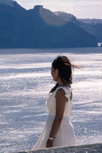 Side view of woman by sea against mountains on sunny day