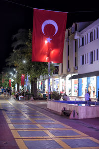 Illuminated street light by road against buildings in city at night