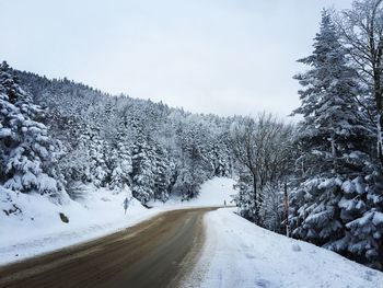 Empty road by snow covered trees against clear sky