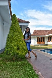 Full length of woman standing by house against sky