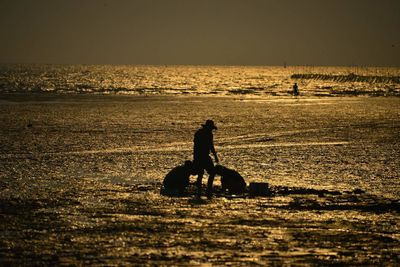 Silhouette people riding on sea against sky during sunset