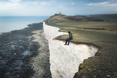 Man on cliff by sea against sky