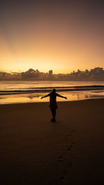 Silhouette woman standing at beach against sky during sunset