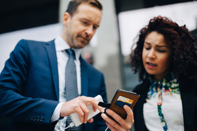 Low angle view of businessman and businesswoman sharing smart phone in city