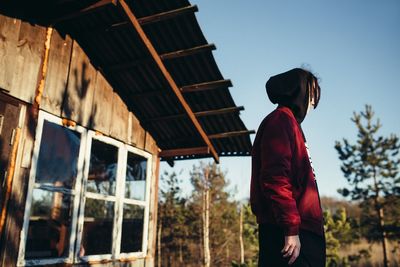 Side view of man wearing warm clothing while standing against house