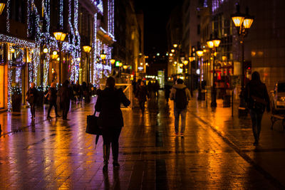 People on illuminated wet street at night