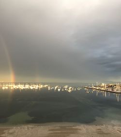 Illuminated city by sea against sky