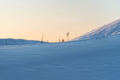 Snow covered landscape against sky during sunset