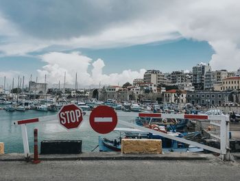 Road sign by buildings in city against sky