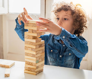 Cute boy stacking wooden blocks on table at home