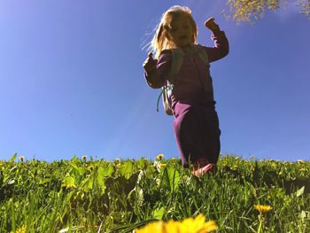 Girl walking on field against clear sky during sunny day