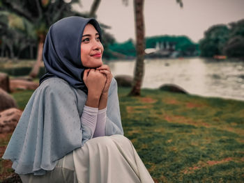 Beautiful young woman sitting by lake