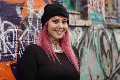 Portrait of smiling woman with pink hair standing against graffiti wall