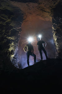 Male tourists exploring cave wearing illuminated headlamps