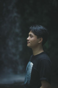 Young man meditating against waterfall