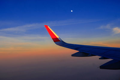 Airplane wing against sky during sunset