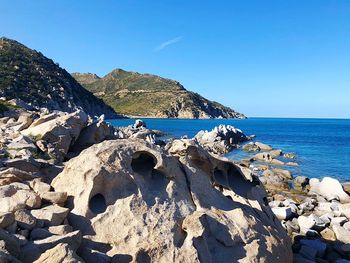 Scenic view of rocks on beach against clear blue sky