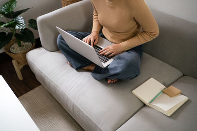 Midsection of woman using laptop while sitting on sofa at home